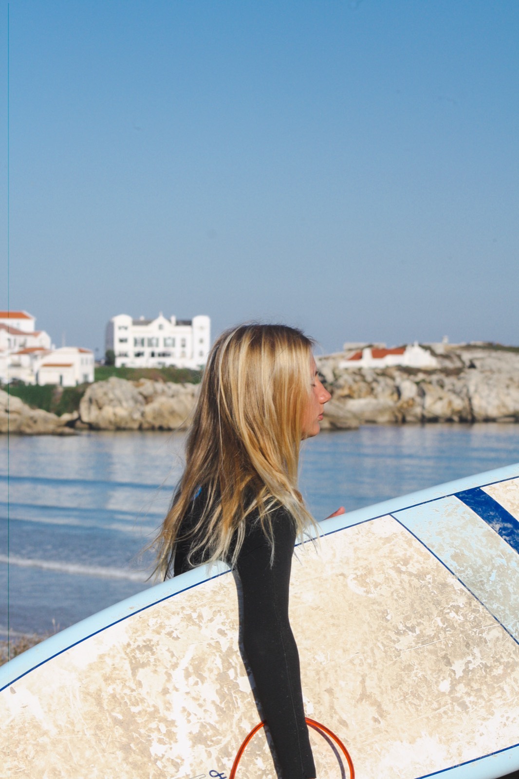 The white houses of Baleal across the water, a surfer in the foreground