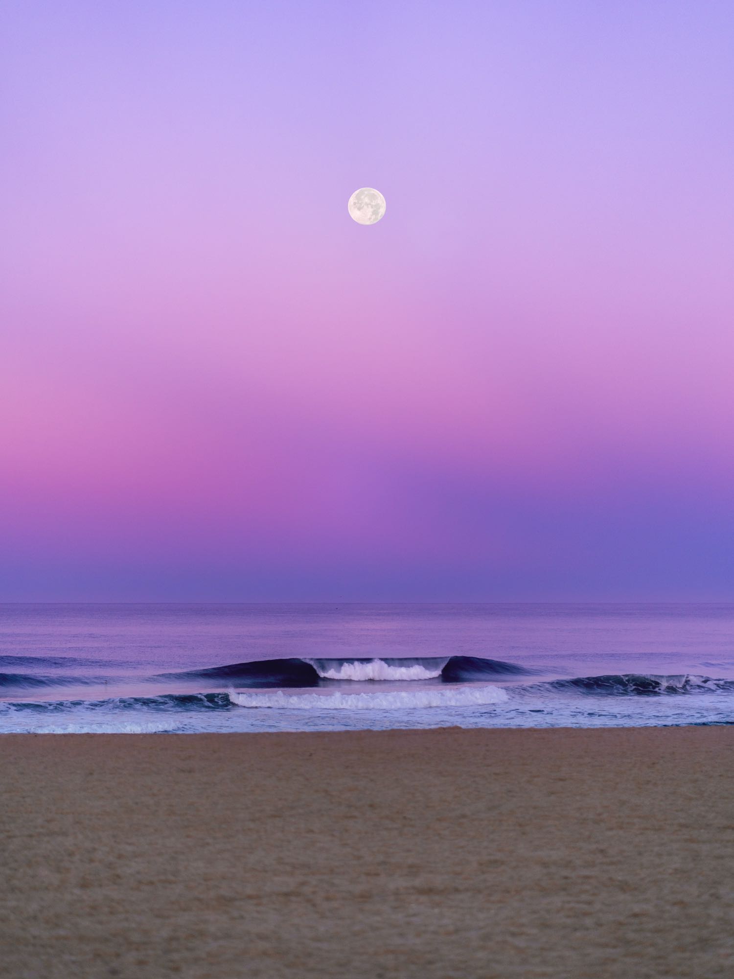 Lines of swell under a violet sky after sunset, seen from the sand.