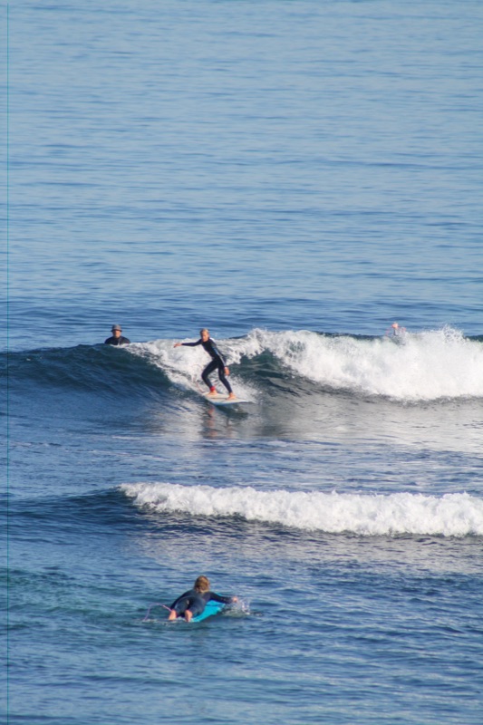 A surfer riding across a clean blue wall with others waiting further out