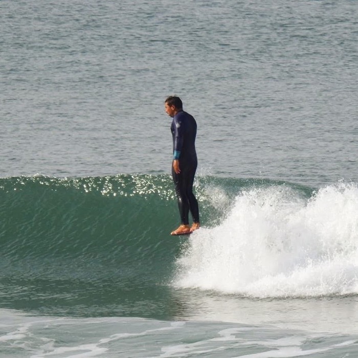 Bruno Grandela riding a longboard with both feet on the nose, on a clean green wall of water.