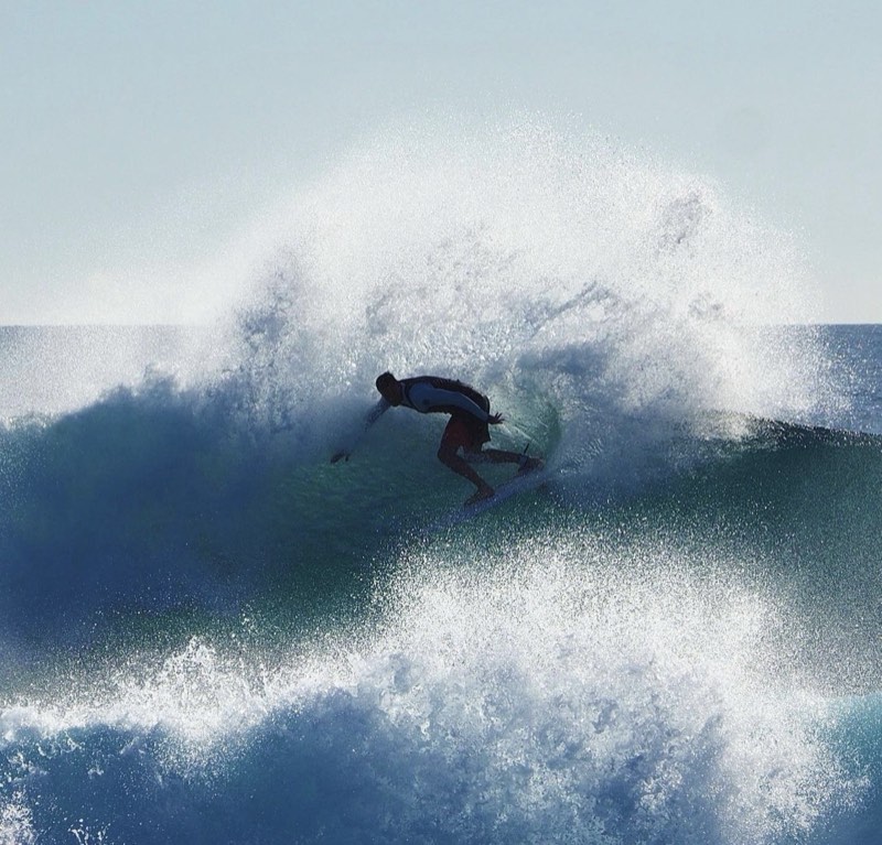 My father surfing backside, throwing a wide fan of spray off the top of a dark blue wave.