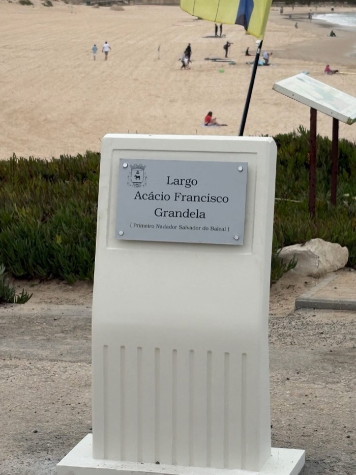 A white stone marker at the entrance to Lagide beach carrying a plaque reading Largo Acácio Francisco Grandela.