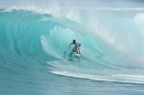 A surfer deep inside a large turquoise barrel, the lip throwing over his head.