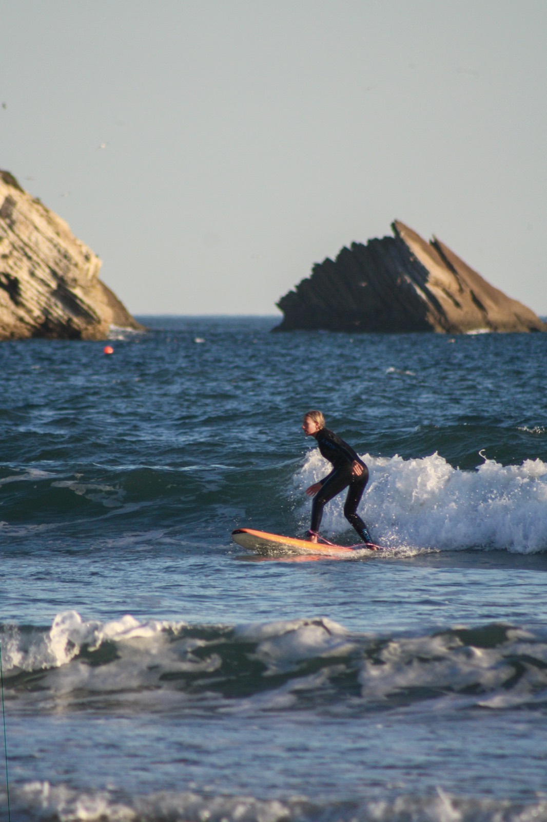 A surfer riding a small wave beneath the rock formations of the coast