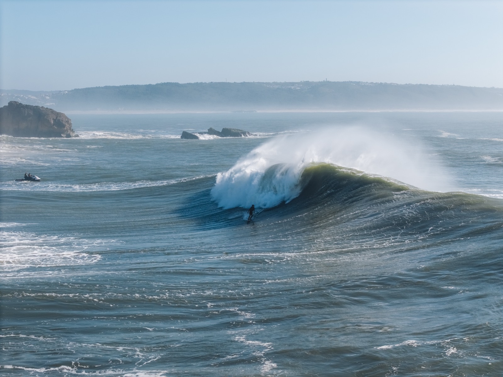 A deep blue Atlantic wave folding over with spray blowing off its lip